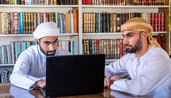 Arabic guys sitting in university library listening to music using headphones