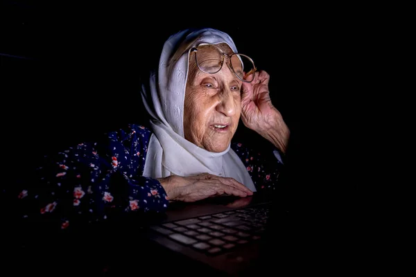 Old woman working on her laptop at midnight in dark room