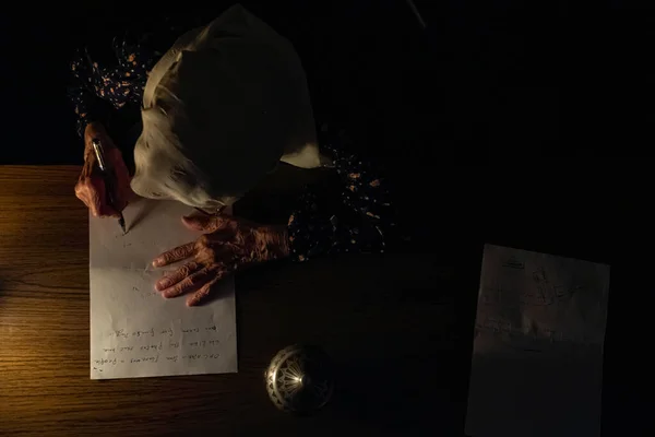 Old lady reading books in dark room with candles light and writing down some notes