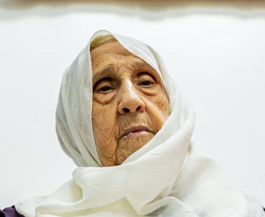 Yaşlı Müslüman kadın yüzünü örtmek için atkısını tutuyor.