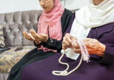 Muslim old woman and her grand daughter using rosary and praying for god clipart