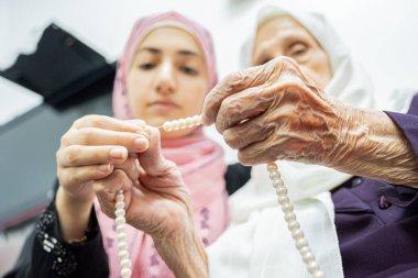 Muslim old woman and her grand daughter using rosary and praying for god clipart
