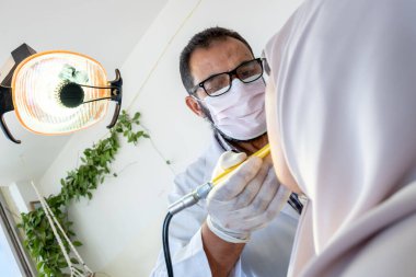 Diş hekimi hastasının dişlerini ağrıdan tedavi ediyor.