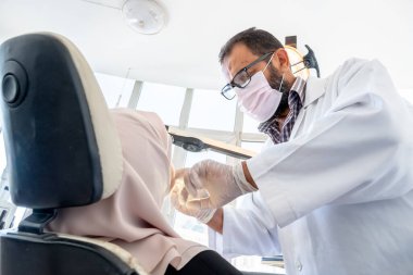 Diş hekimi hastasının dişlerini ağrıdan tedavi ediyor.