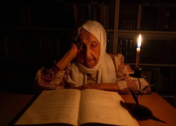 Arabic muslim old woman reading books in her library at night with candles light