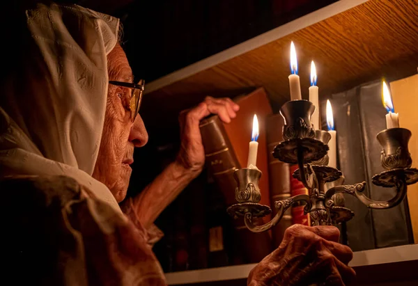 Arabic muslim old woman reading books in her library at night with candles light