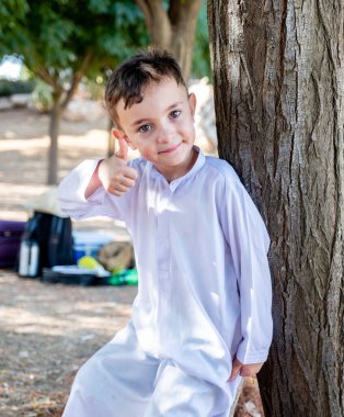 Mutlu Arap çocuk ağaçların yanında dikiliyor ve başparmak kaldırıyor