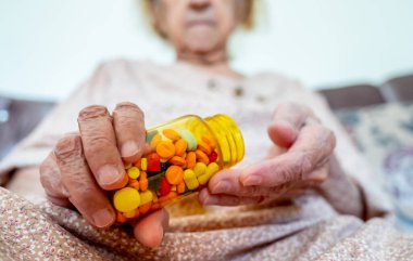 Yaşlı kadın ilaçlarını elinde tutuyor.