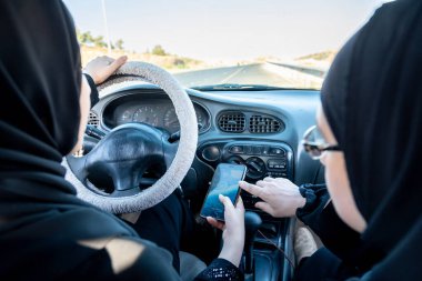 Biri telefonla konuşurken iki Arap kadın araba kullanıyor.