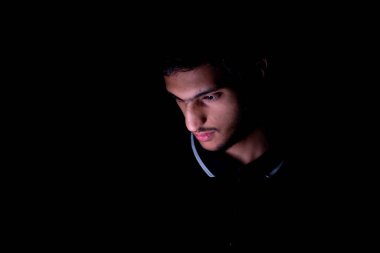 Ortadoğulu bir adamın karanlık bir odada telefonunu kontrol ederken portresi.