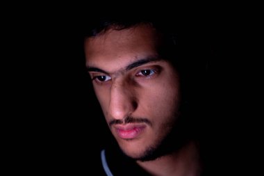 Ortadoğulu bir adamın karanlık bir odada telefonunu kontrol ederken portresi.