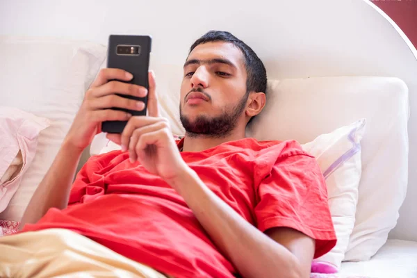 Muslimský Chlapec Leží Posteli Dívá Svůj Telefon — Stock fotografie