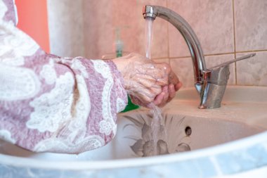 Yaşlı kadın ellerini yıkıyor.