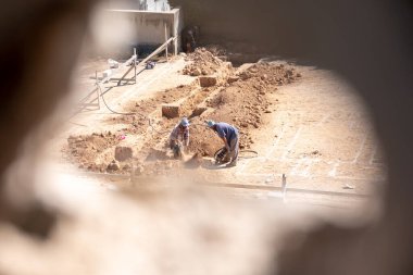 Kompresör kullanılarak mahalledeki tasarıma göre yeni bir evin temellerini kazan işçiler için bir delikten geçen bir fotoğraf.