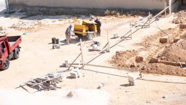 İşçiler kompresör kullanılarak mahalledeki tasarıma göre yeni bir evin temellerini kazıyorlar.