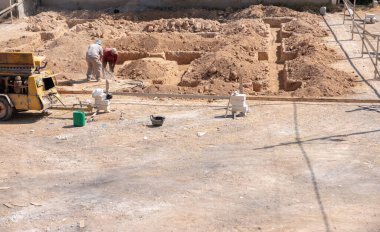 İşçiler kompresör kullanılarak mahalledeki tasarıma göre yeni bir evin temellerini kazıyorlar.