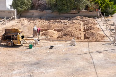 İşçiler kompresör kullanılarak mahalledeki tasarıma göre yeni bir evin temellerini kazıyorlar.