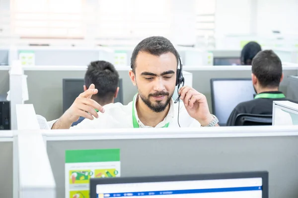 Young man working at a computer in a call centre ,with his colleagues