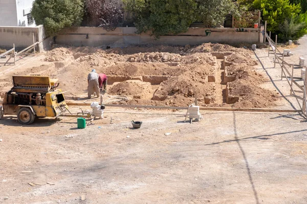 İşçiler kompresör kullanılarak mahalledeki tasarıma göre yeni bir evin temellerini kazıyorlar.