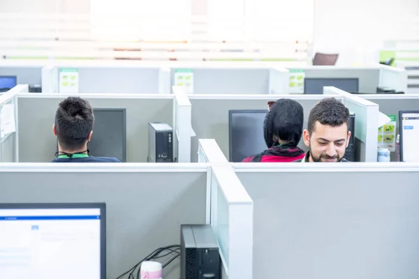 Young man working at a computer in a call centre ,with his colleagues