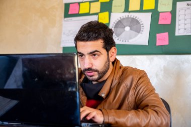 Genç adam evinde yüksek konsantrasyonlu işiyle meşgul. Ofisinde yapışkan bir tahtayla dizüstü bilgisayarını kullanıyor.