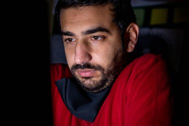 Genç adam çalışırken karanlıkta laptopunun önünde üşüyor.