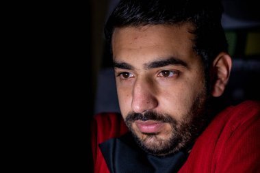 Karanlık odada monitör önünde genç bir adam için gizli bir yüz.