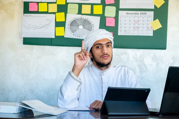 Young arabian man is making a live video from his office in front of his laptop