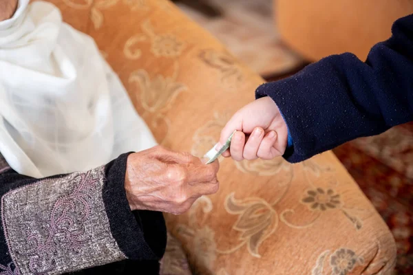 Yaşlı kadının elleri Arabistan bayramı sırasında torununa para veriyor.