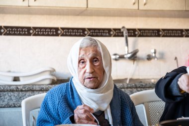 Yaşlı kadın mutfakta yemek yiyor.