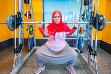 Arap Müslüman kadın tesettür takıyor. Formda, atletik ve sağlıklı olmak için çömelme eğitimi alıyor.