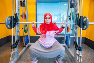 Arap Müslüman kadın tesettür takıyor. Formda, atletik ve sağlıklı olmak için çömelme eğitimi alıyor.