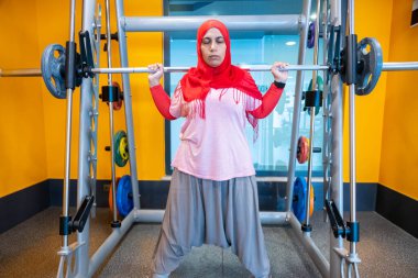 Arap Müslüman kadın tesettür takıyor. Formda, atletik ve sağlıklı olmak için çömelme eğitimi alıyor.