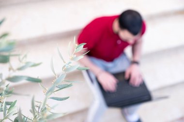 Arap adam dışarıda dizüstü bilgisayar kullanıyor ve merdivenlerde oturuyor.