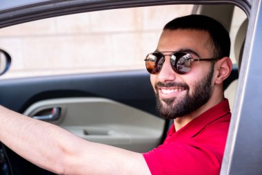 Arap adam gülümseyerek ve kendinden emin bir şekilde arabasını sürüyor.
