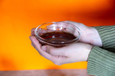 Kadın elleri turuncu arka planda bir kase bal tutuyor.