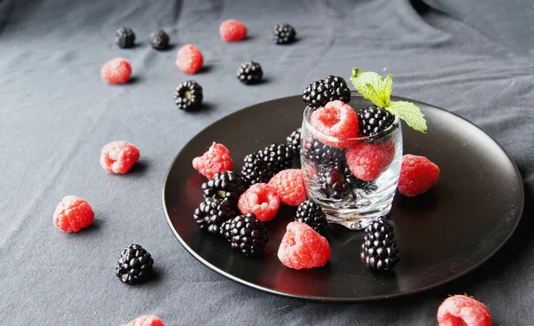 Чорні ягоди і малини в склянці — стокове фото