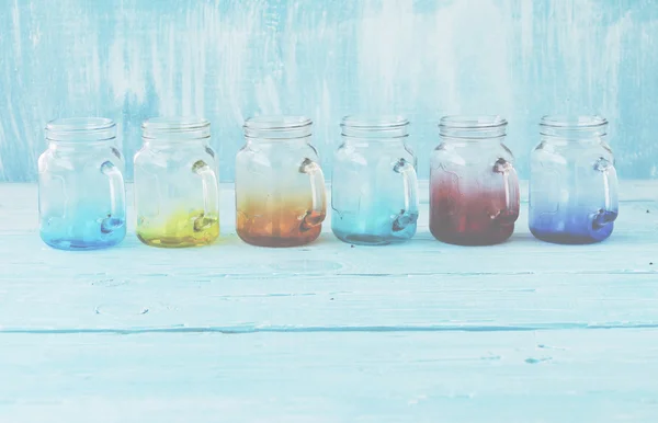 Kolorowe szklane słoiki z uchwytami na niebieskim tle drewnianych — Zdjęcie stockowe