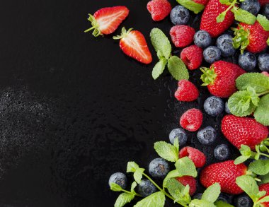 taze çilek, ahududu ve siyah bir arka plan üzerinde yaban mersini