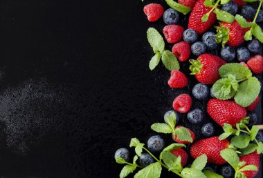 taze çilek, ahududu ve siyah bir arka plan üzerinde yaban mersini