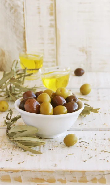 Чорно-зелені оливки, оливкова олія на білому дерев'яному столі — стокове фото