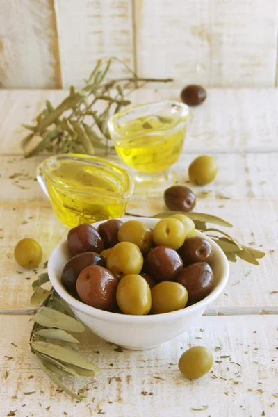 Чорно-зелені оливки, оливкова олія на білому дерев'яному столі — стокове фото