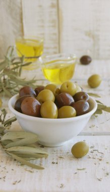 Beyaz ahşap bir masa üzerinde siyah ve yeşil zeytin, zeytin yağı
