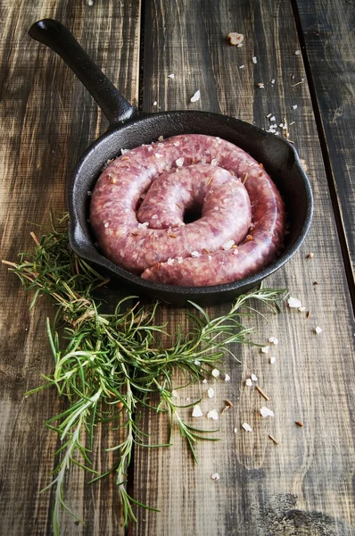 Biberiye ve Baharatlar, ahşap masa, seçici odak ile dökme demir tavada üzerinde çiğ Dana sosis