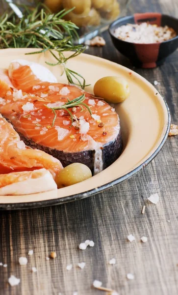 Raw salmon steak on an enamel plate with rosemary and spices, wooden table, selective focus — Stock Photo, Image