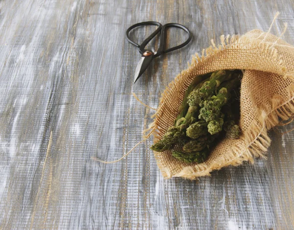 Asparagus in a canvas bag with pair of scissors on wooden table, selective focus — Stock Photo, Image