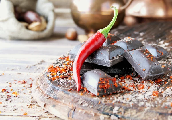 Pieces of chocolate with chili peppers on a wooden table — Stock Photo, Image