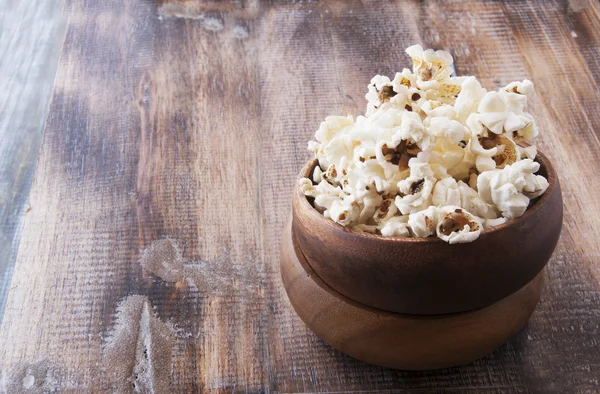 Palomitas de maíz en un plato de madera en el fondo — Foto de Stock