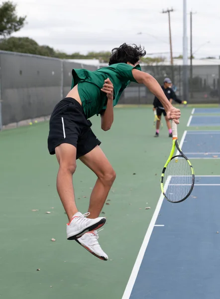 Young boys and girls volleying and serving in a tennis match