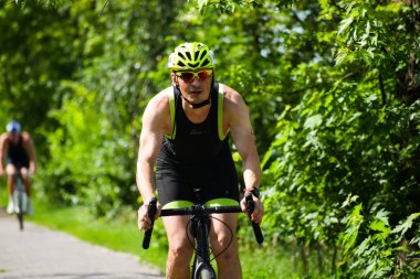 POLTAVA, UKRAINE - 19 Haziran 2021: Bisikletçiler yaz öğleden sonraları triatlon yarışmaları sırasında parkta bisiklet sürerler